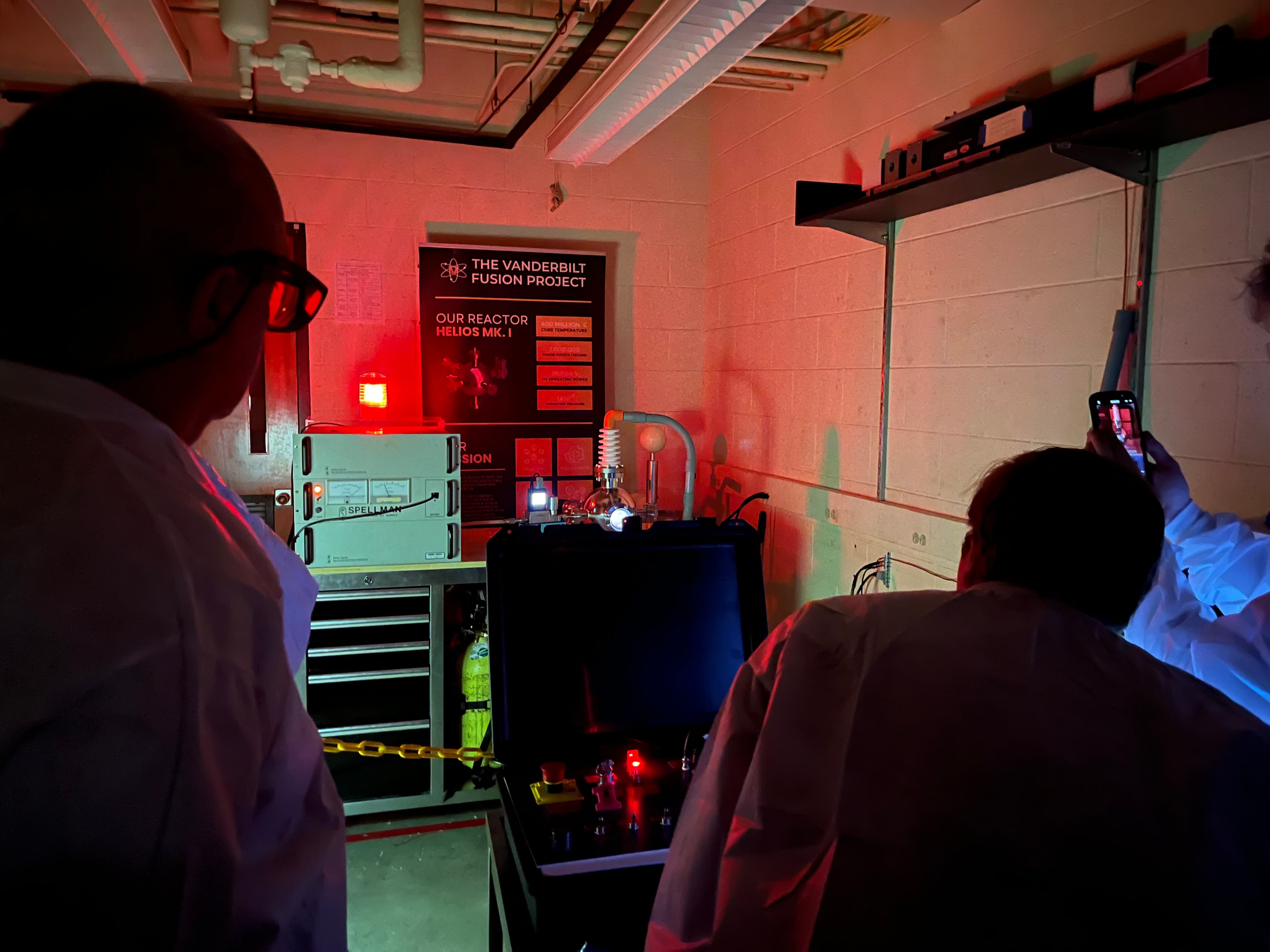 Reactor operations room under red safety lighting; team members watching HELIOS Mk. 1 during a run